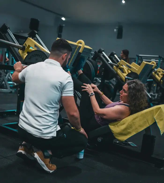 Personal trainer che assiste un’atleta durante l’esercizio di leg press.